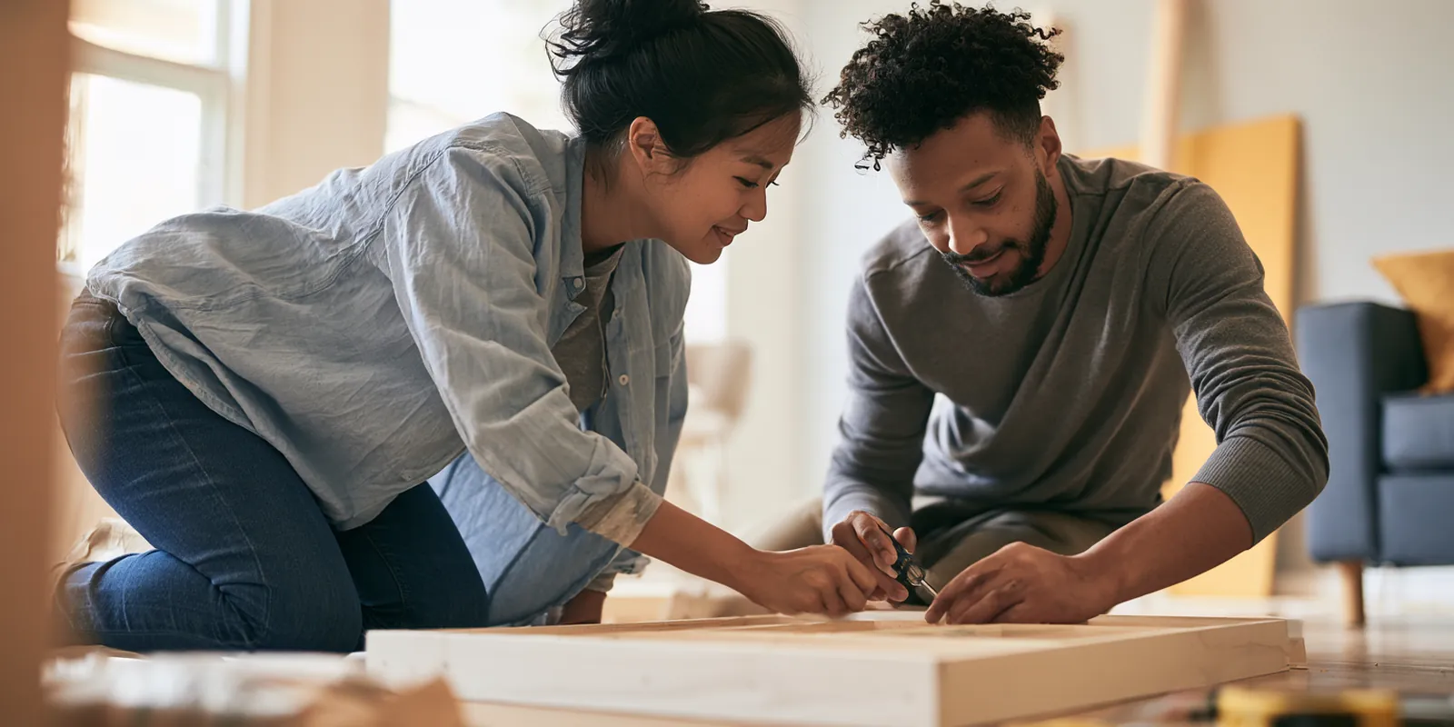 Couple in their 30s assembling a new bookshelf on the living room floor, a purchase they might cover with avant lending or a card