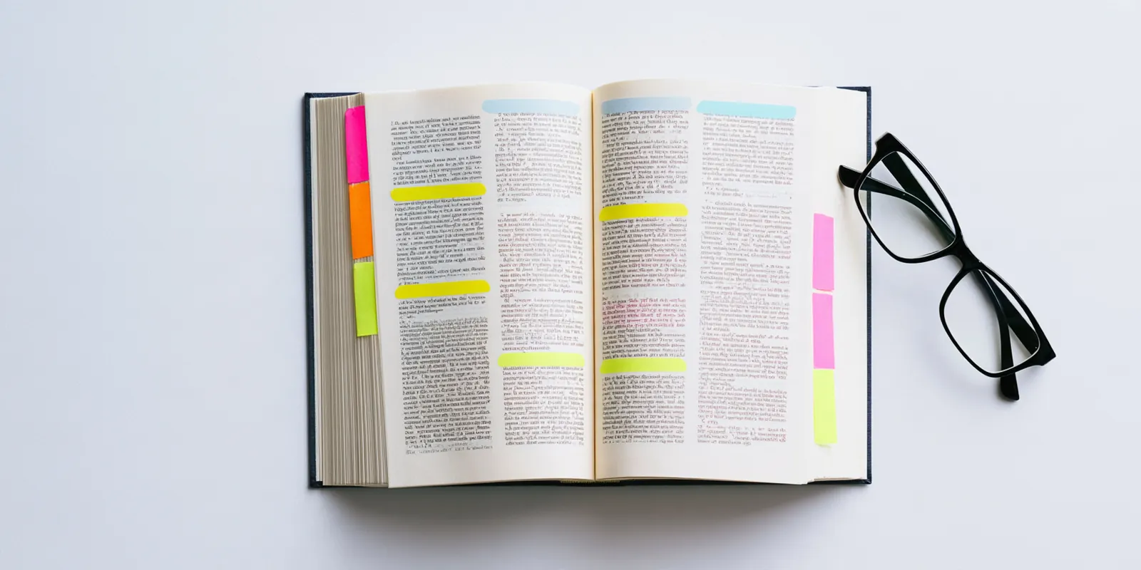Open hardcover book with colorful sticky tabs marking pages beside a pair of reading glasses, like a reference guide to avant lending terms