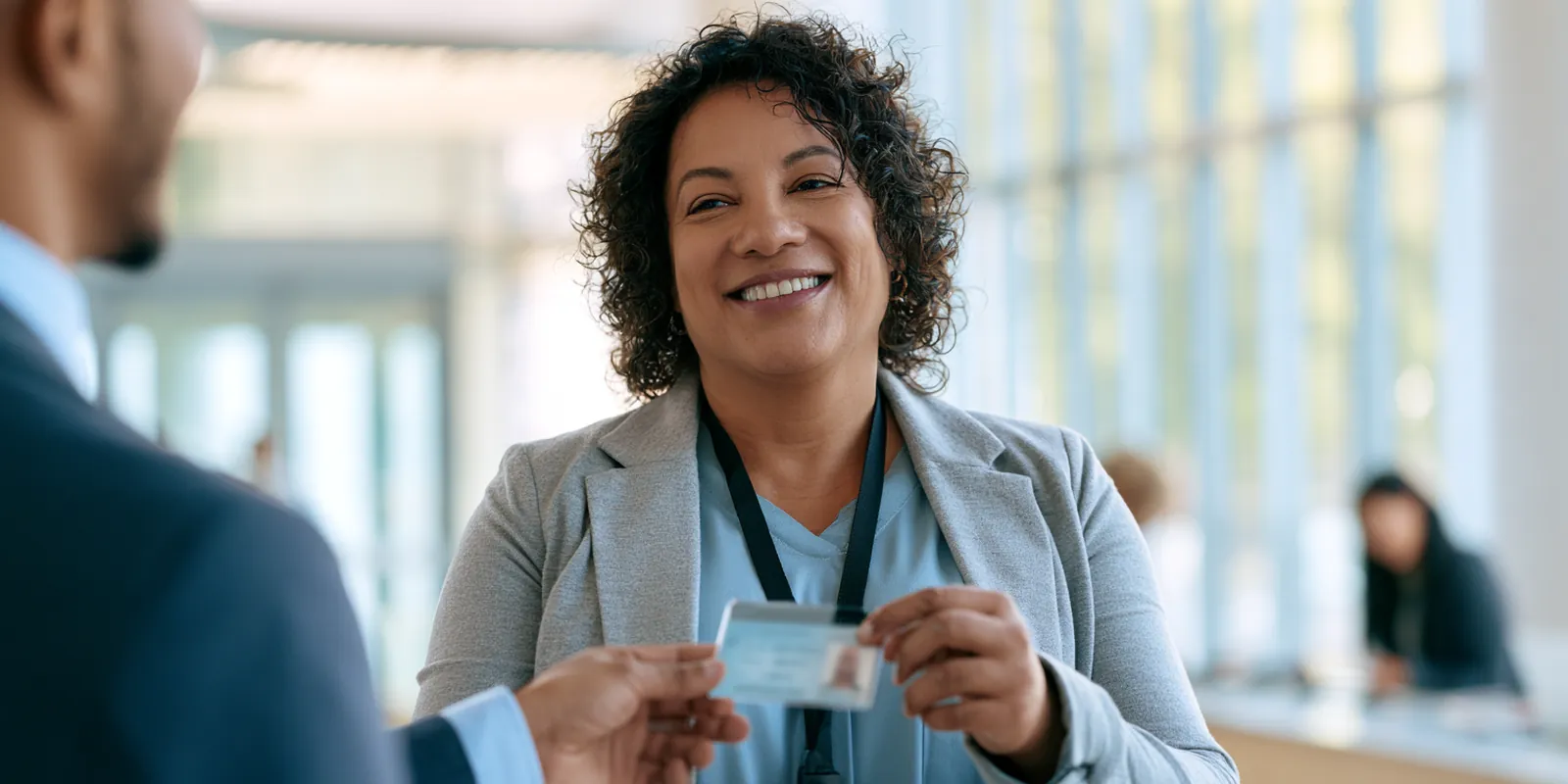 HR specialist in her 50s handing a new hire his ID badge in a bright office lobby, steady income that helps avant lending eligibility