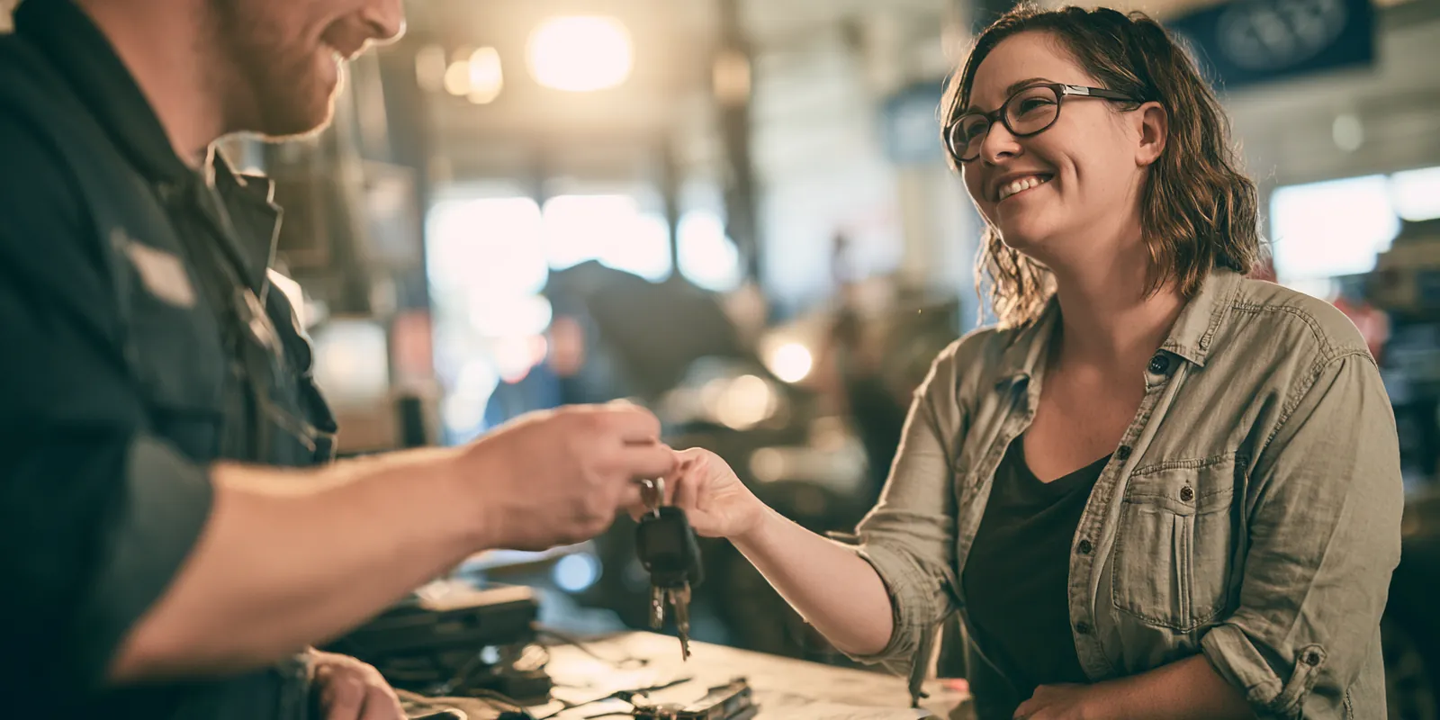 Mechanic returning car keys to a woman in her 30s across the counter of a bright auto shop after a repair covered by a $2,000 loan