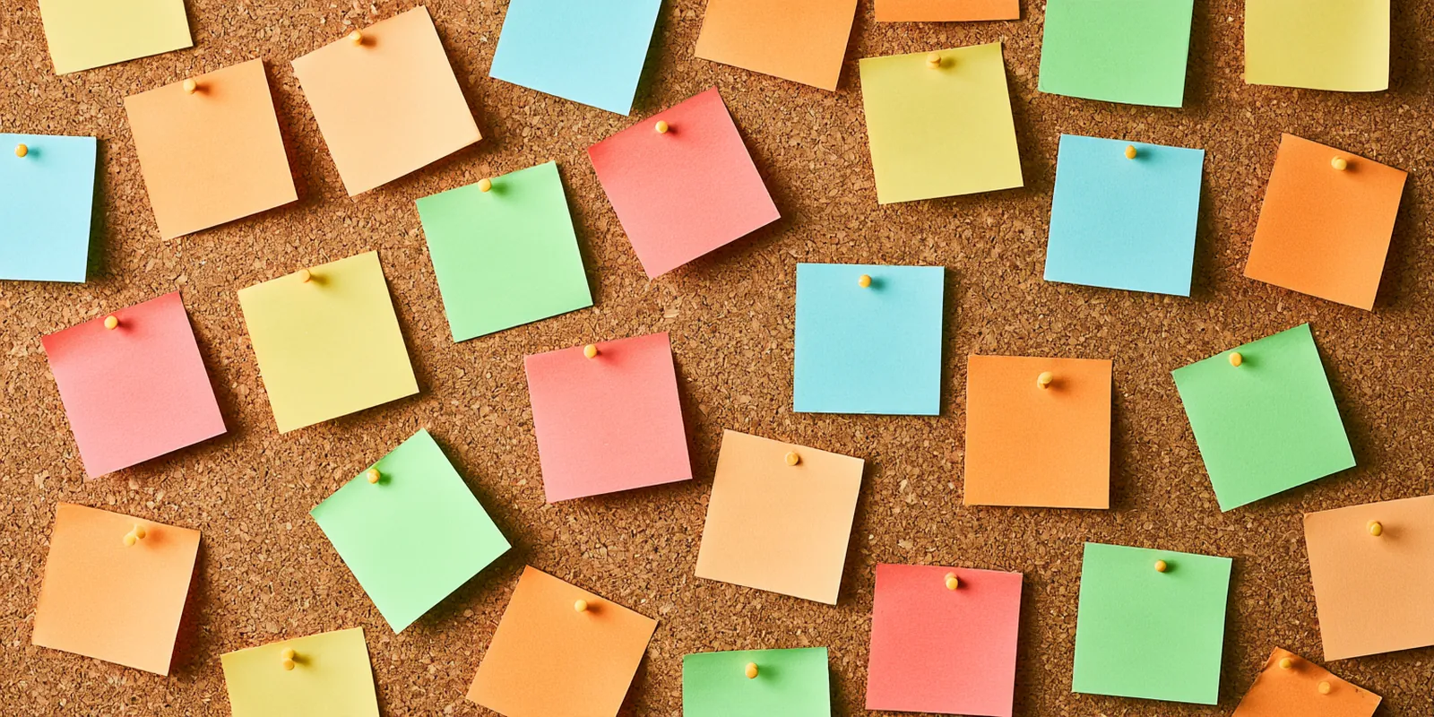Top-down view of a cork pinboard covered with colorful index cards and round pins, like an avant lending debt payoff plan laid out on a table