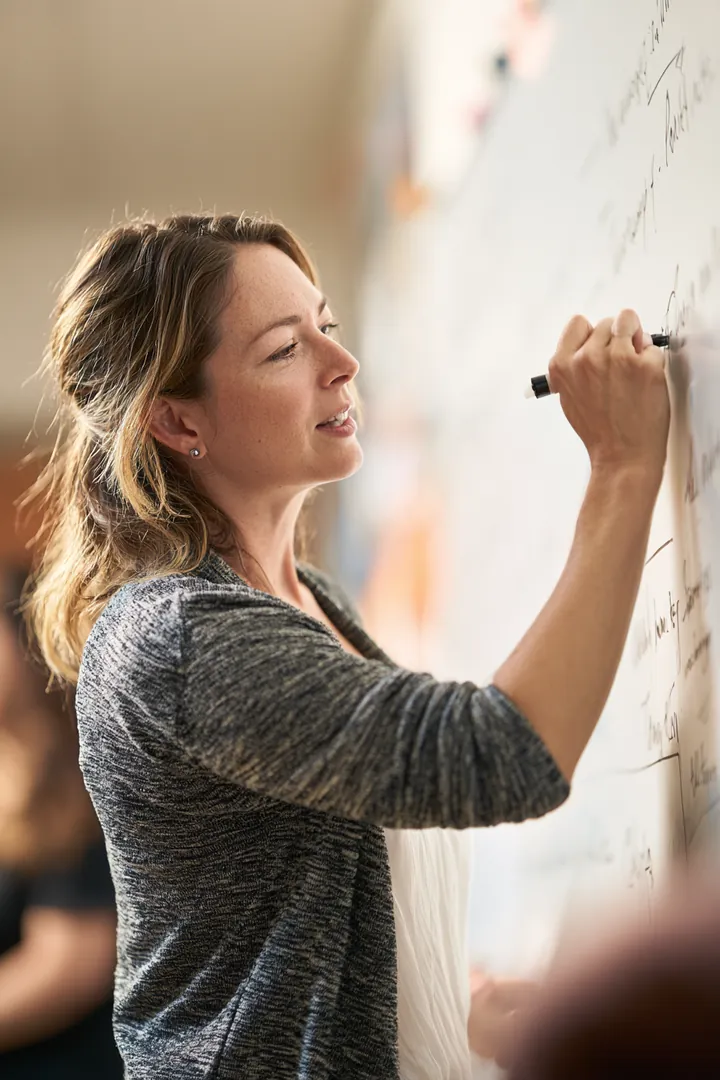 Woman in her 40s writing key finance terms on a whiteboard while teaching a community evening class